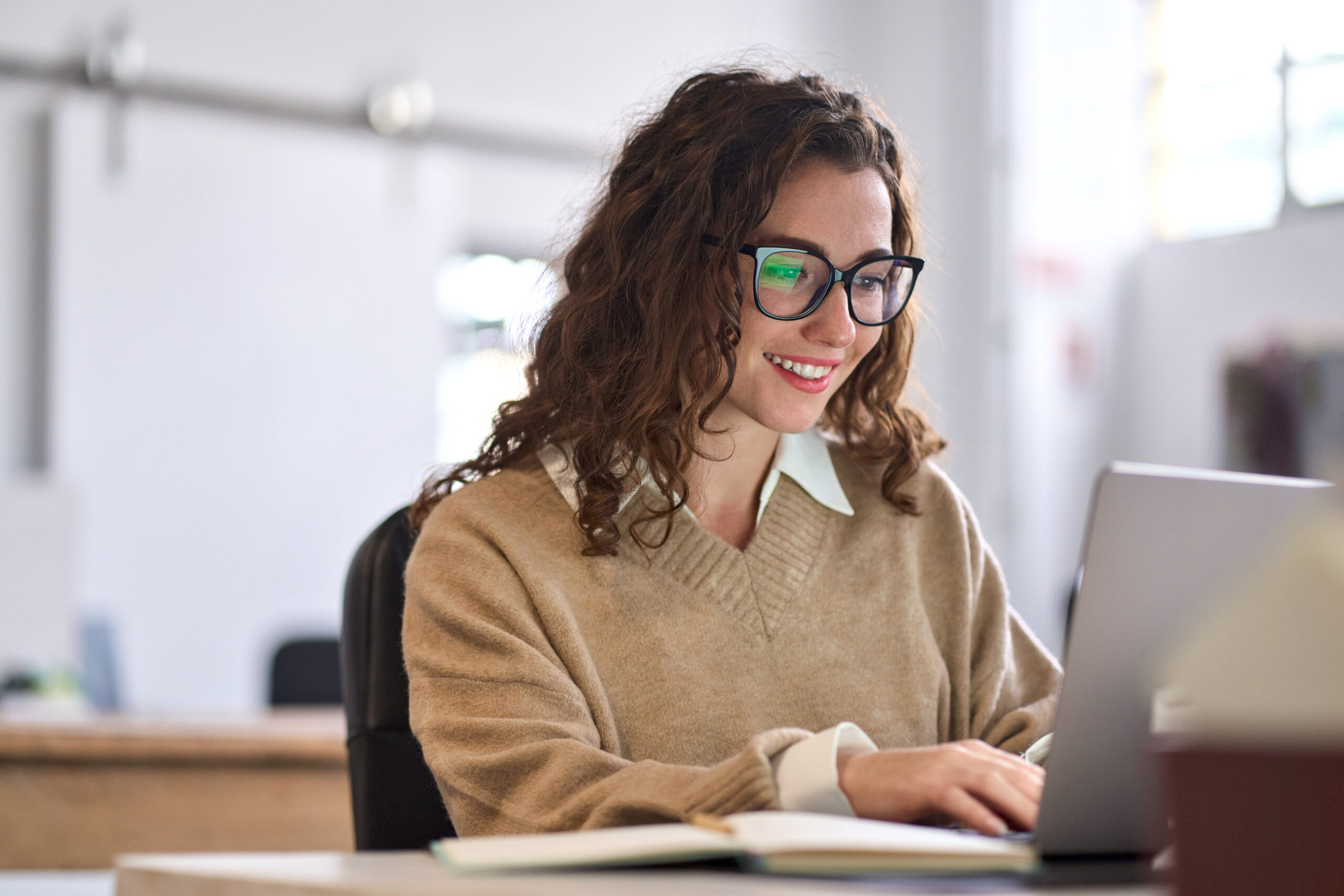 Young happy woman employee or student sitting at desk using laptop.