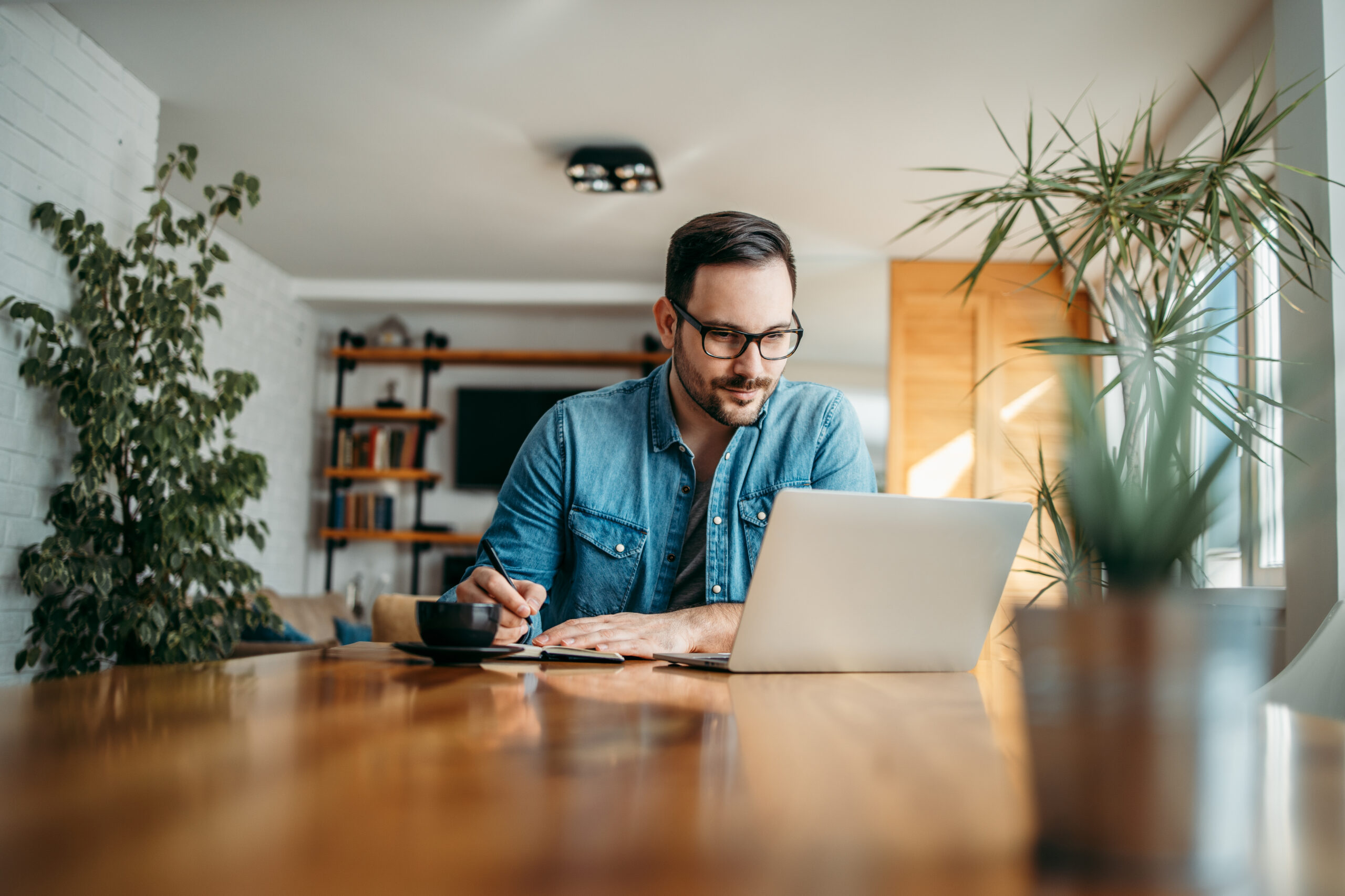 Handsome man taking notes and looking at laptop, at home office, portrait.